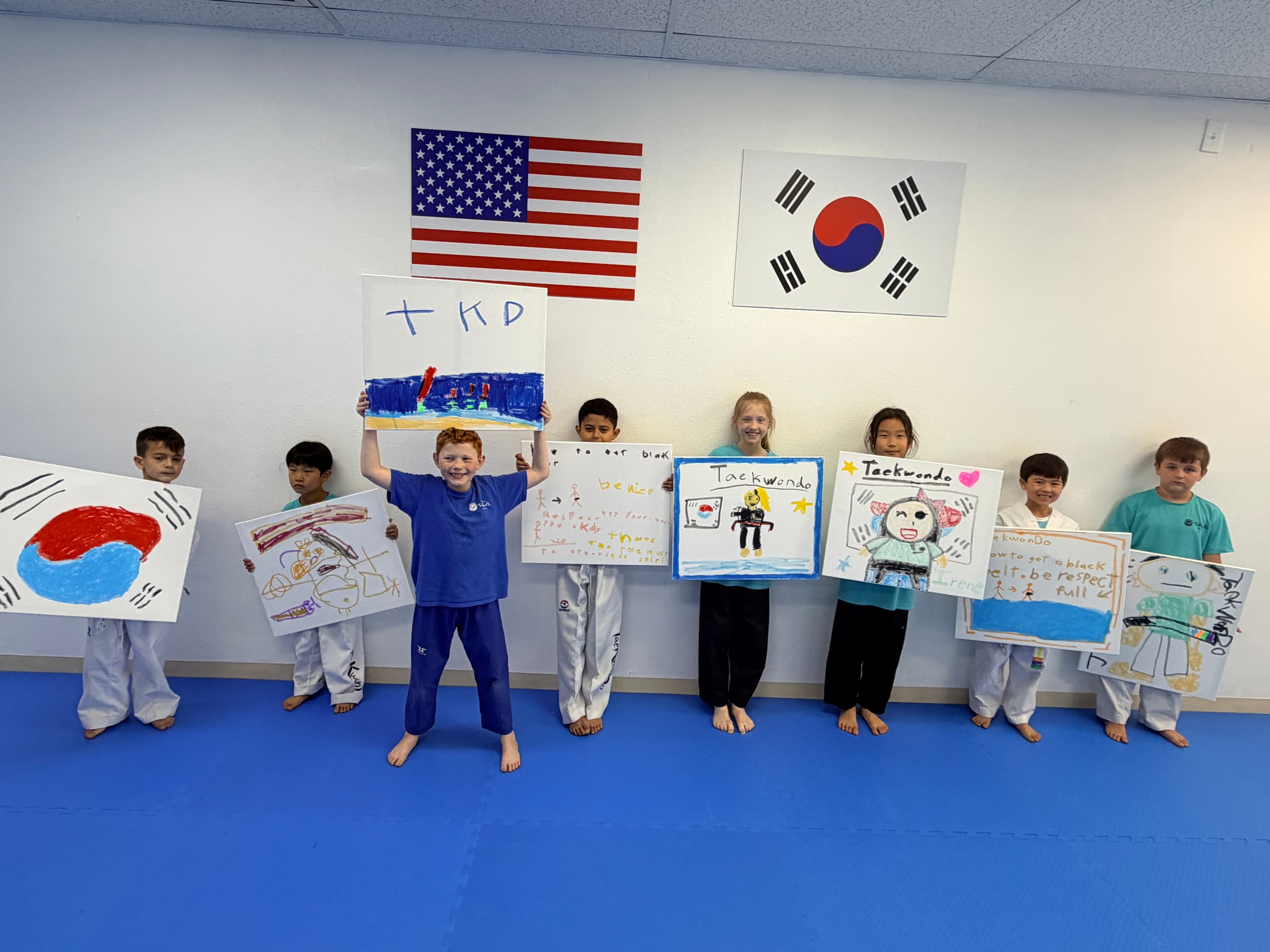 Students holding their Taekwondo paintings beneath the American and Korean flags