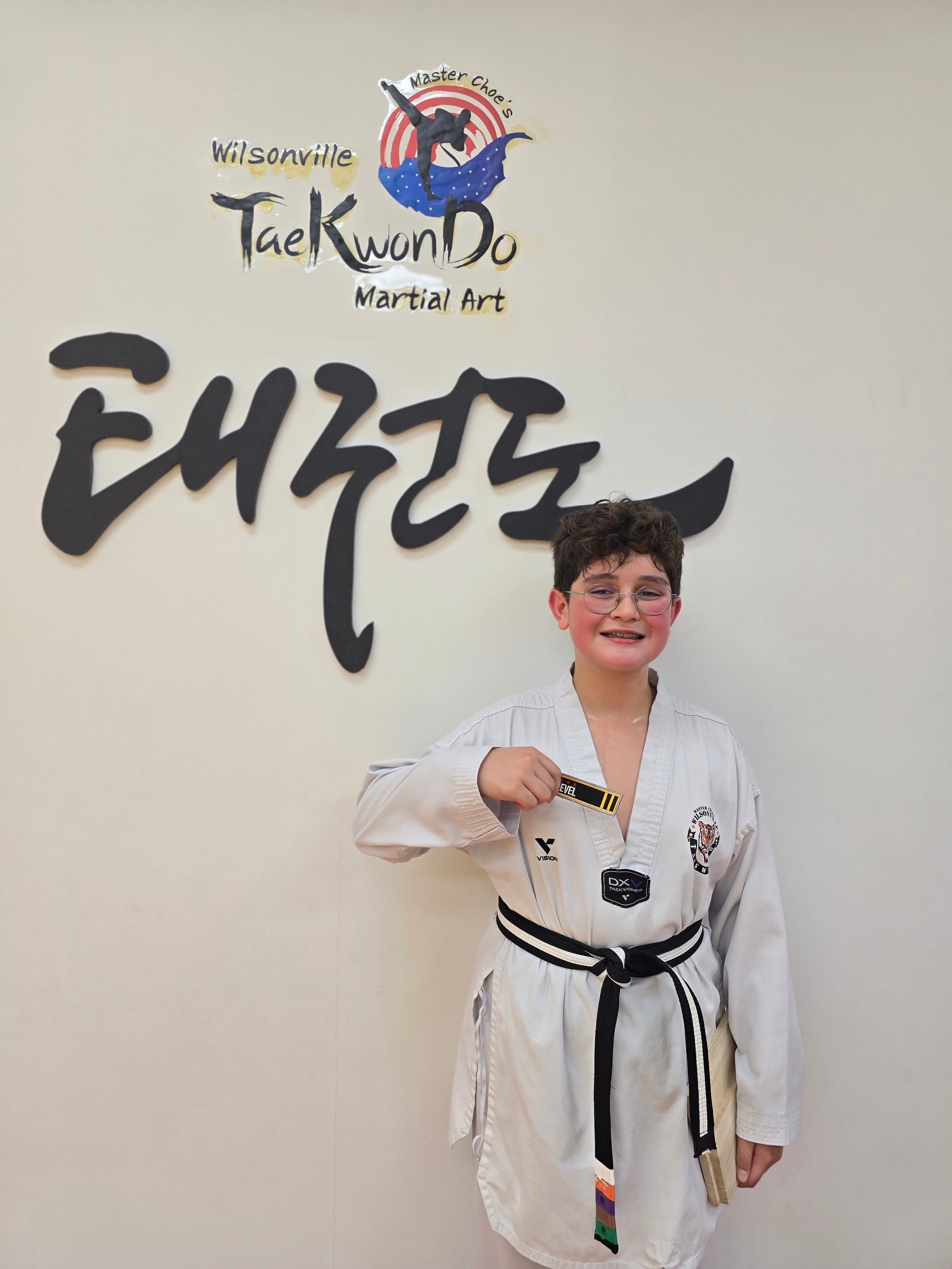 Student proudly holding his new black belt level tag in front of the academy logo