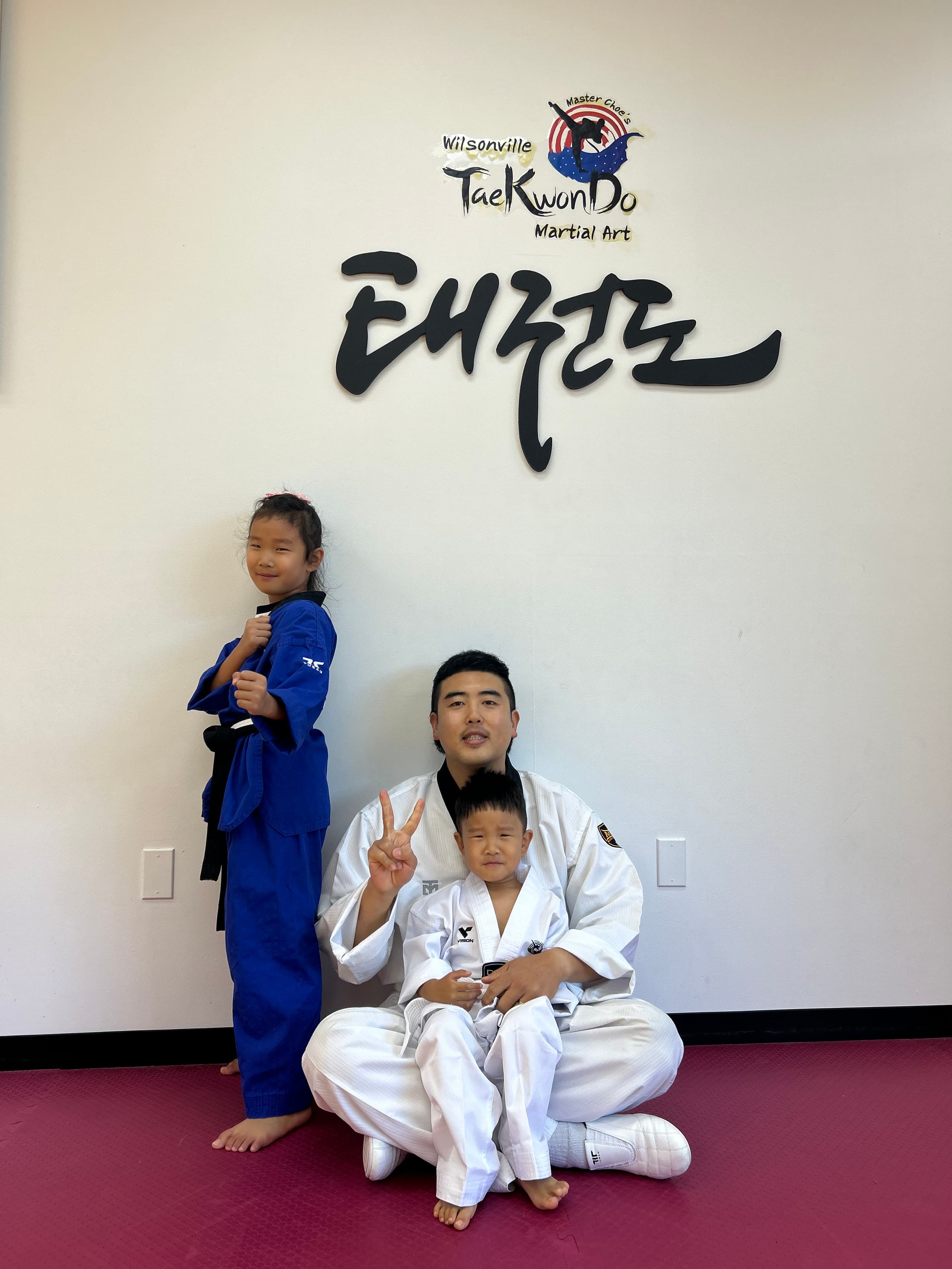 Master Choe sitting with two young students beneath the academy logo