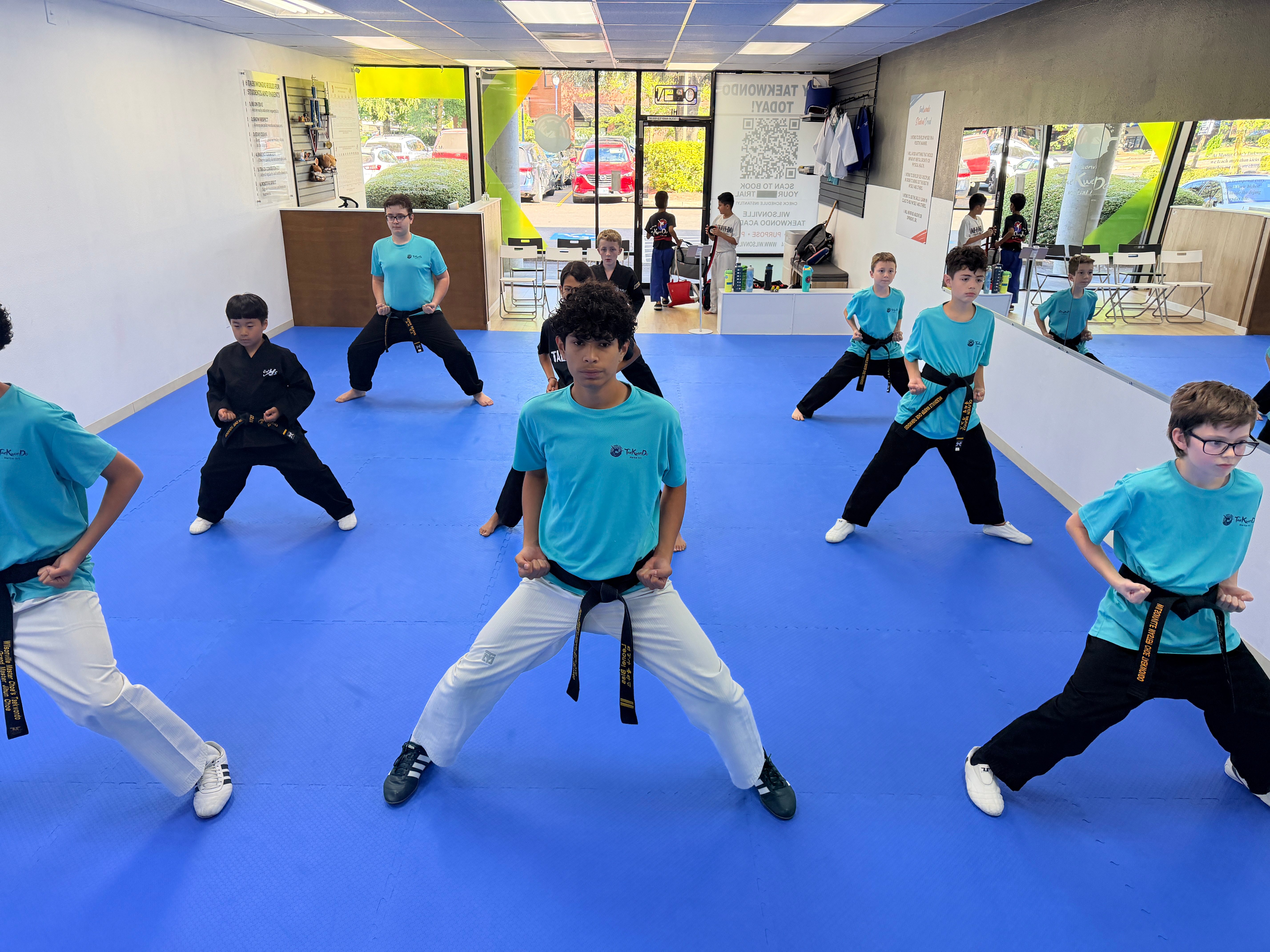 Black belt students practicing a low stance together on the blue mat inside the Wilsonville academy