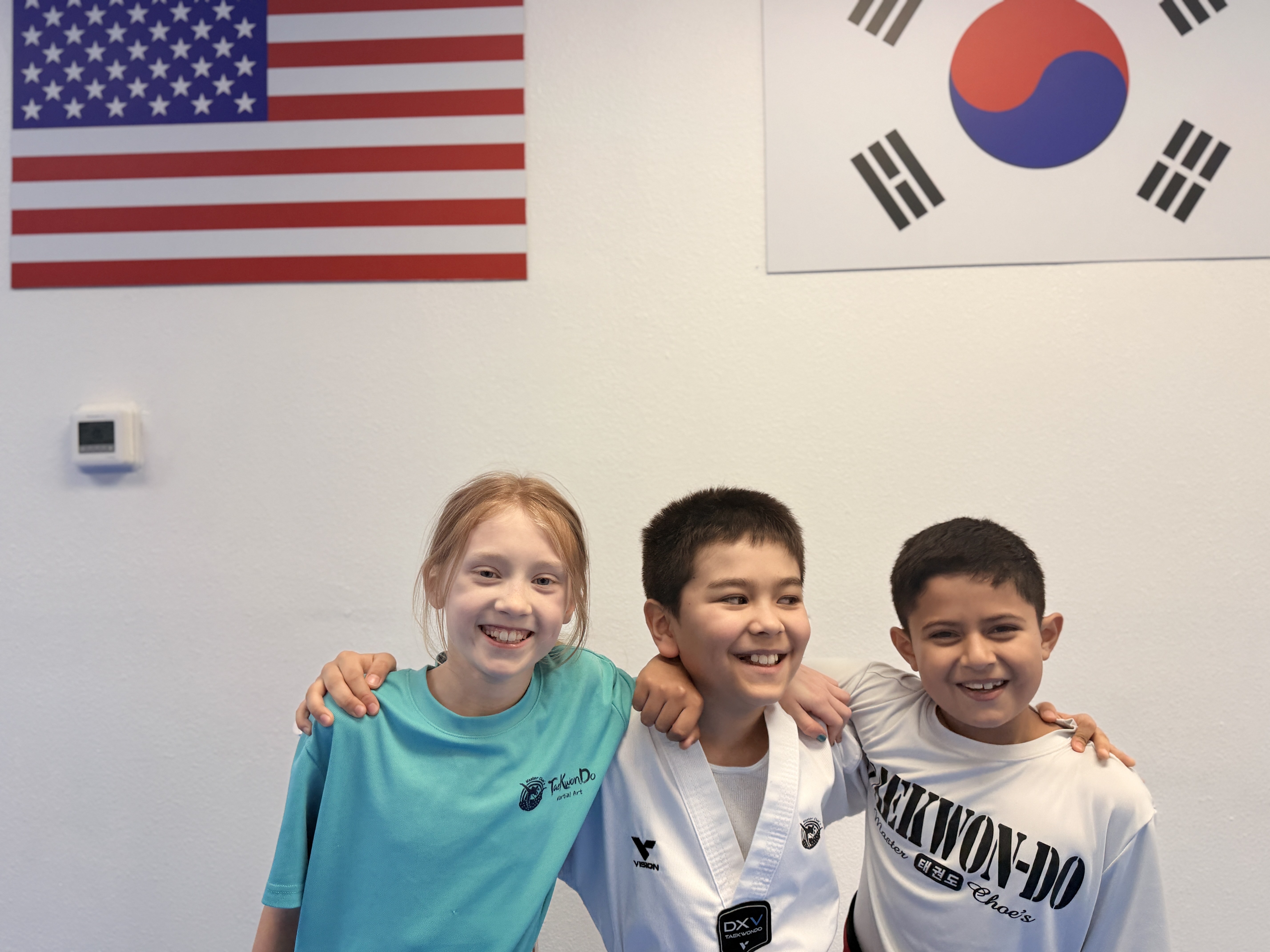 Three smiling students arm in arm under the American and Korean flags
