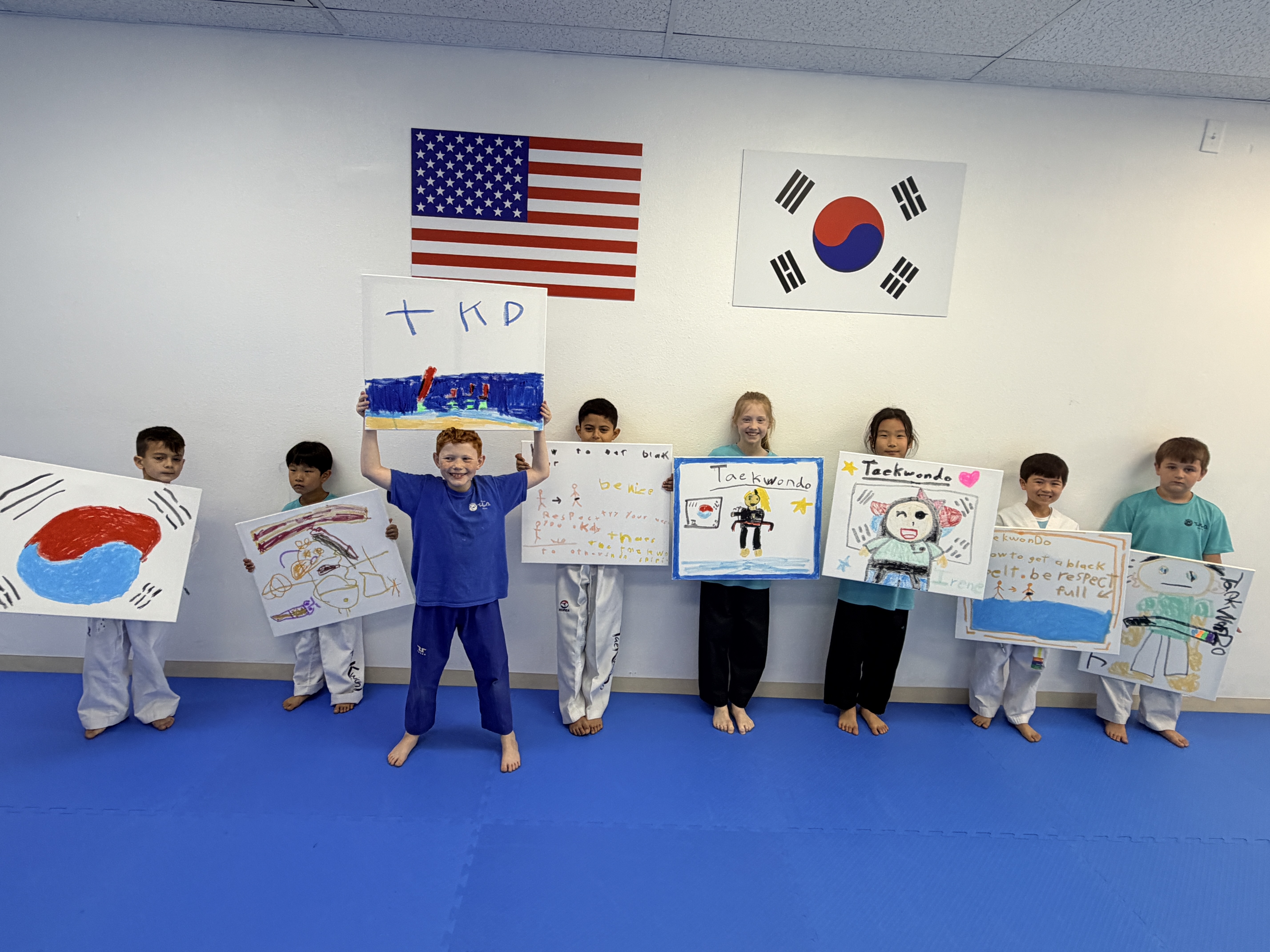 Students proudly holding their taekwondo drawings in front of the flags