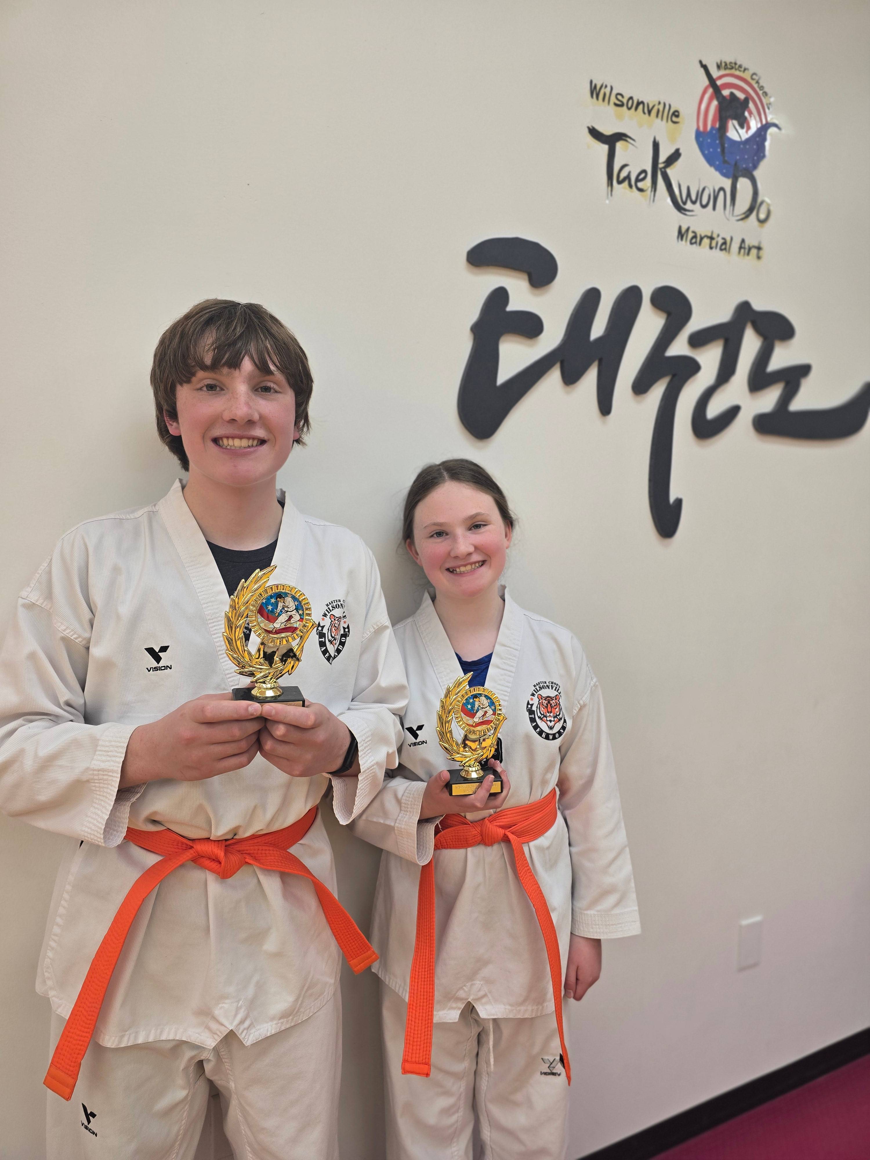 Two teen orange belt students holding trophies